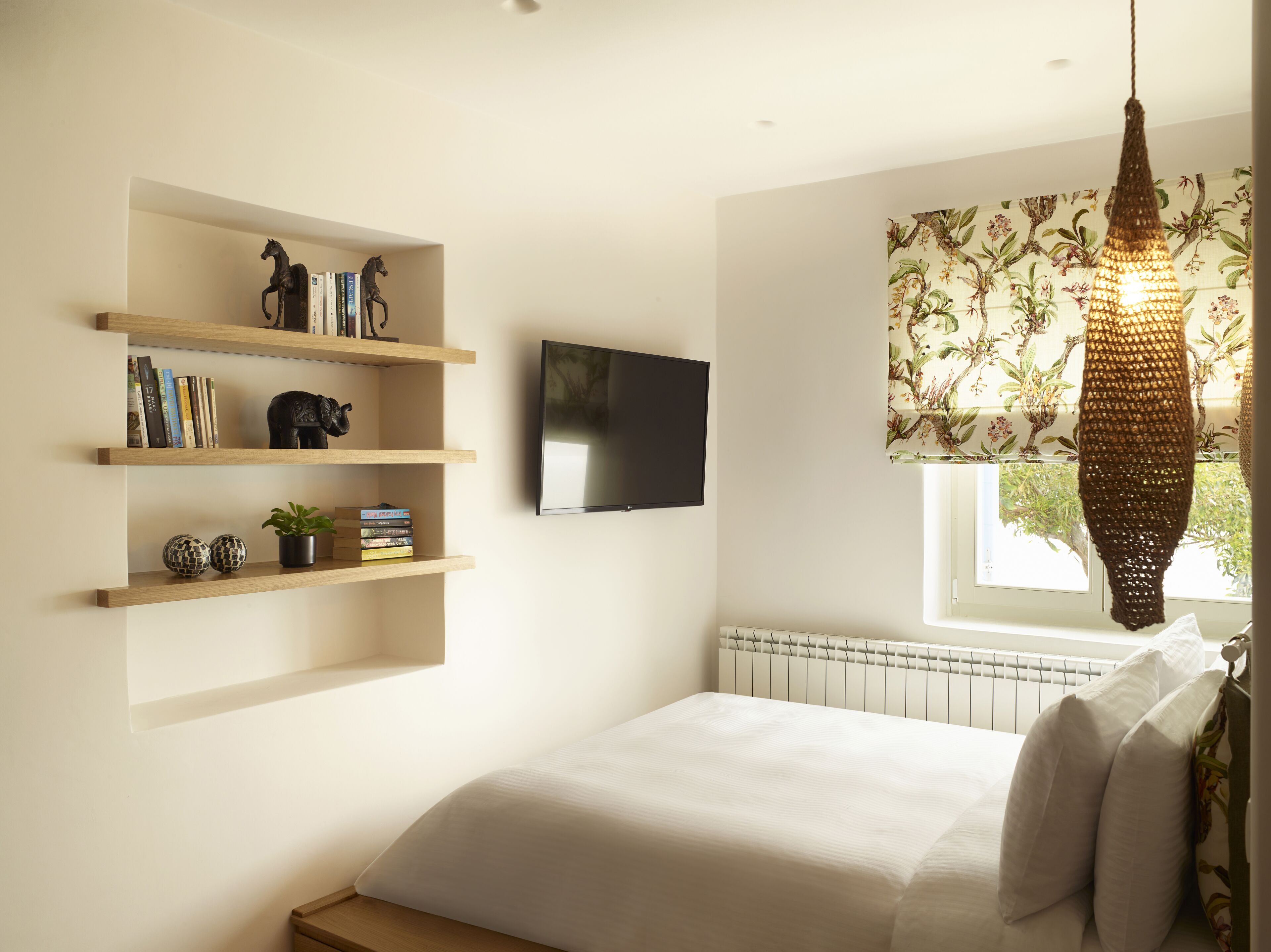 Une chambre à coucher avec un lit, un téléviseur fixé au mur et une fenêtre avec un rideau.