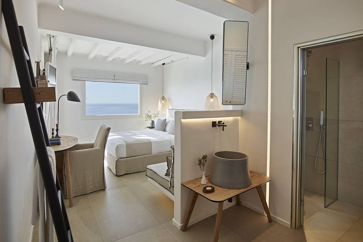Een moderne hotelkamer met een bed, een bureau, een douche en uitzicht op zee.