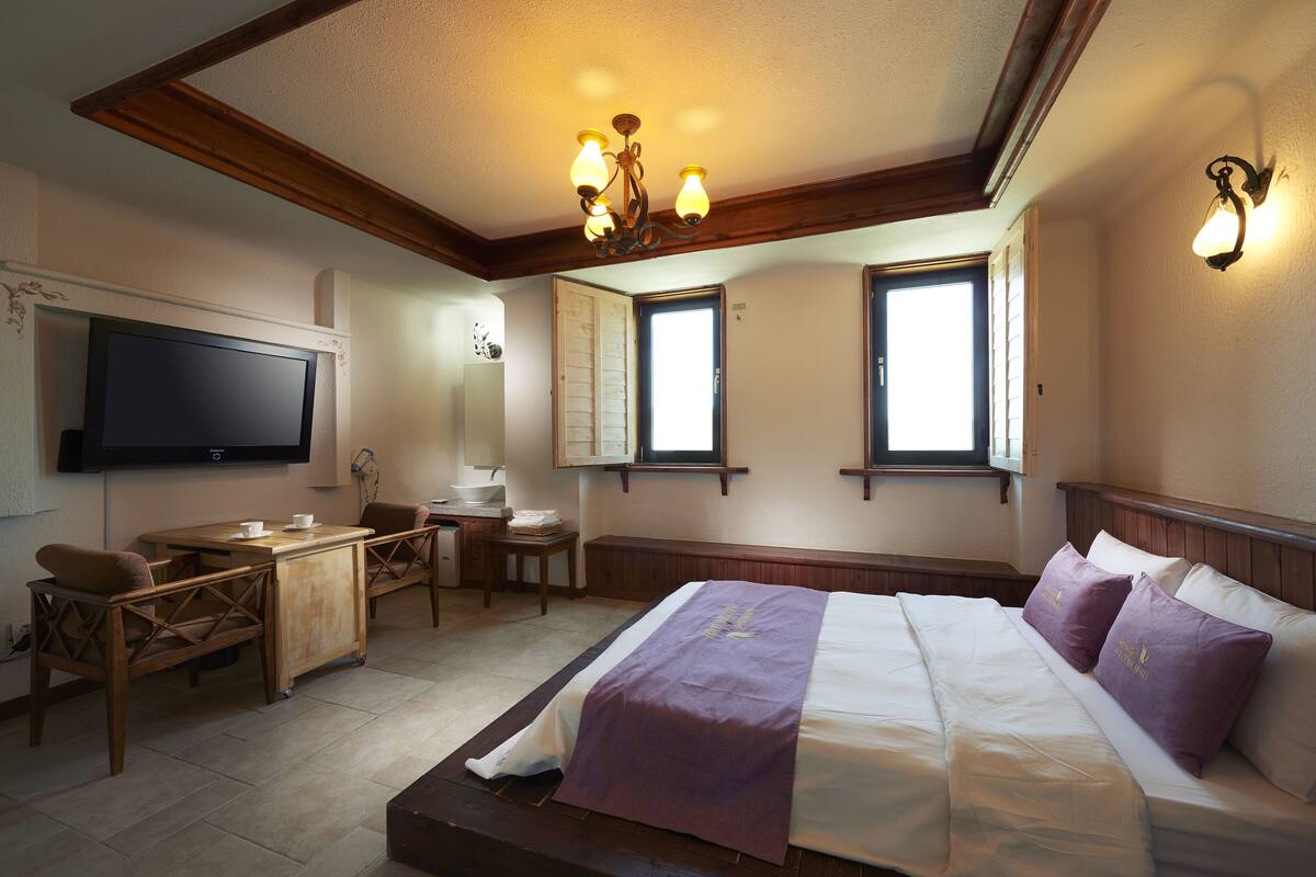 A hotel room with a bed, a desk, a chair, a television, and a window.