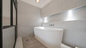 Ein modernes Badezimmer mit einer freistehenden Badewanne, gefliesten Wänden und einem sichtbaren Lüftungsgitter am Boden.