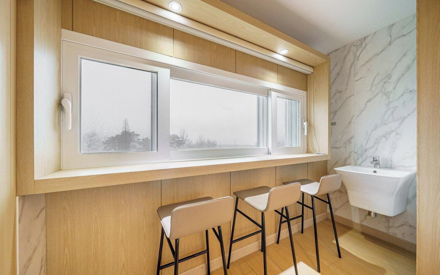 A modern bathroom with a large window, a sink, and three bar stools.