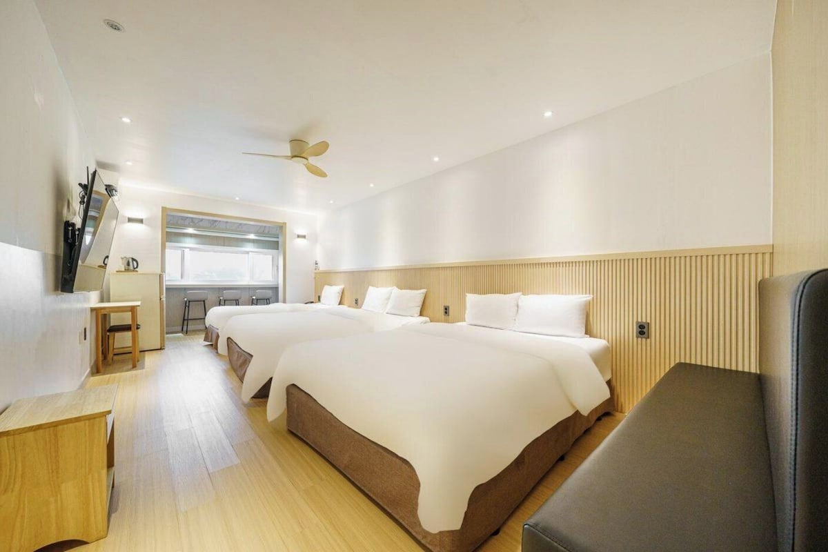 Een hotelkamer met twee bedden, een bureau, een stoel, een plafondventilator en een raam.