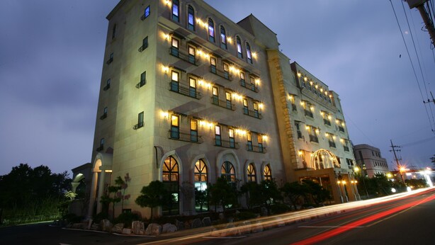 A multi-story hotel with illuminated windows and balconies, featuring a classic architectural style with arched windows and a central entrance. - Incheon Airport Hotel Oceanside (Incheon)