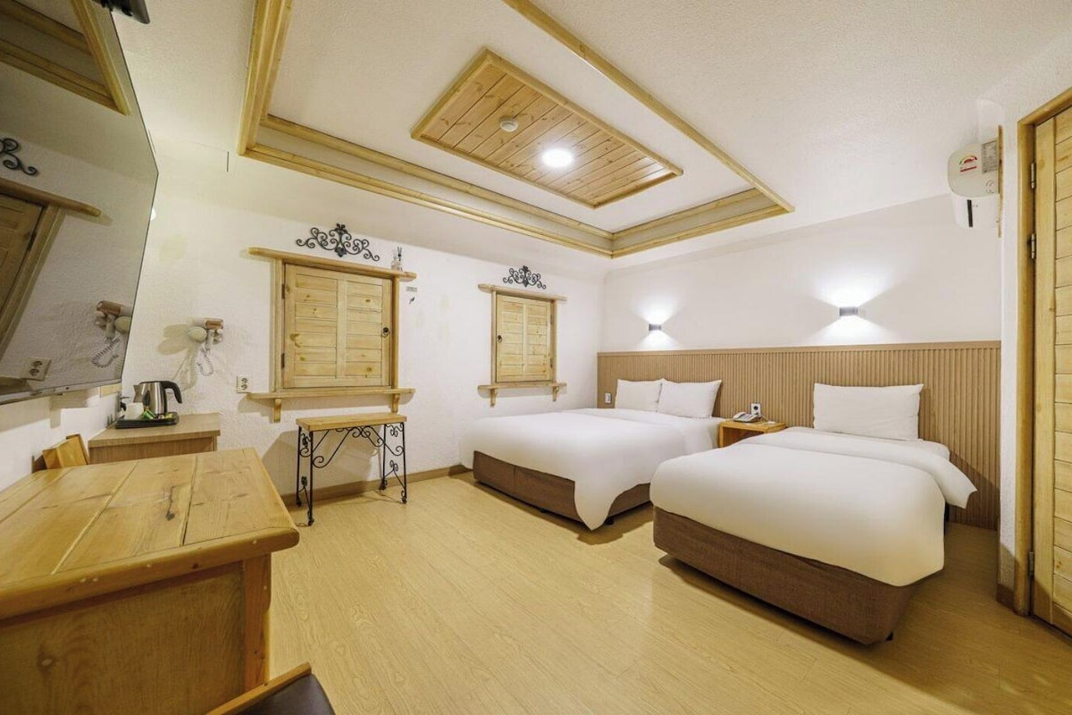 Een hotelkamer met twee bedden, een houten tafel, een klein bureau en een plafondventilator.