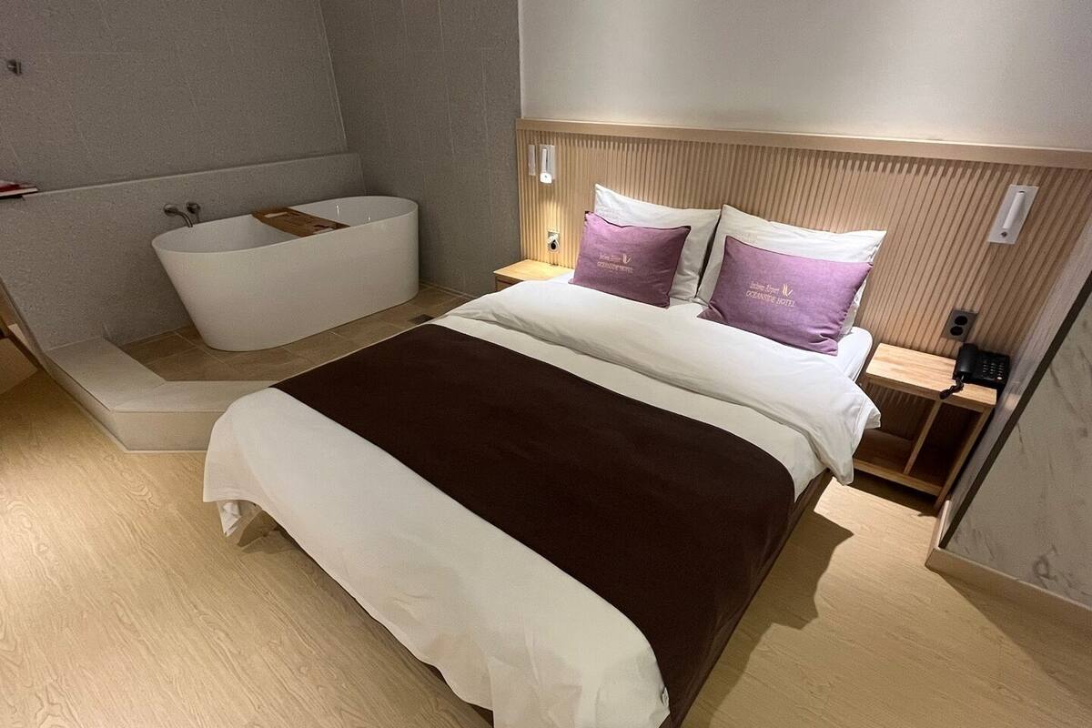 A modern hotel room with a large bed, a built-in bathtub, and a wooden headboard.