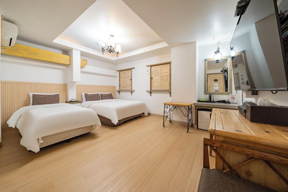 A hotel room with two beds, a wooden table, a small table, a mirror, and a ceiling light.