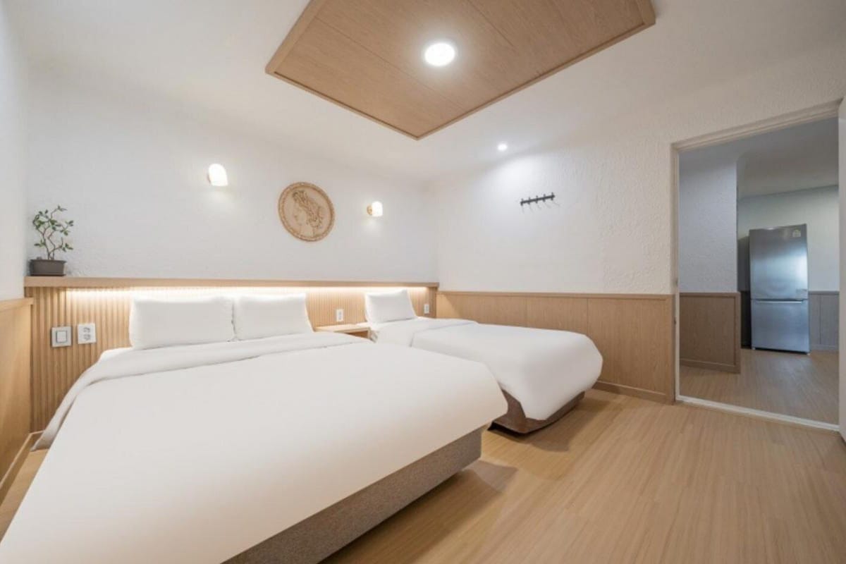 Een hotelkamer met een groot bed, een klein nachtkastje, een wandlamp en uitzicht op de keuken.