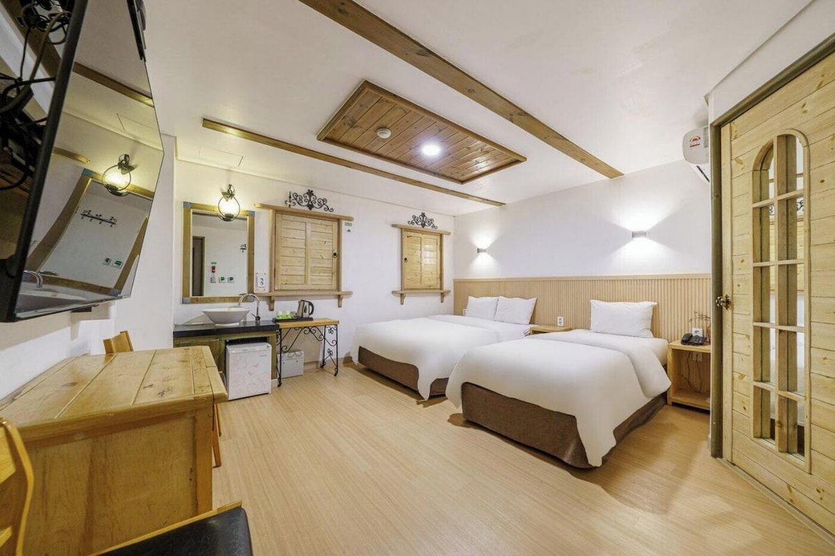 Een hotelkamer met twee bedden, een houten eettafel, een kitchenette en een grote spiegel.