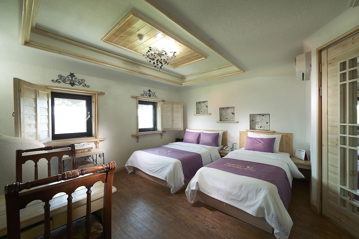 A room with two beds, wooden furniture, a ceiling fan, and a window with shutters.