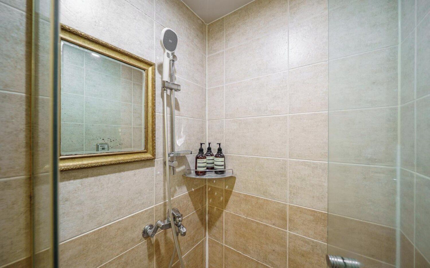 A bathroom with a shower, a mirror, and a shelf with toiletries.