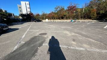 A parking lot with a shadow of a person, a BMW car, and a building in the background.