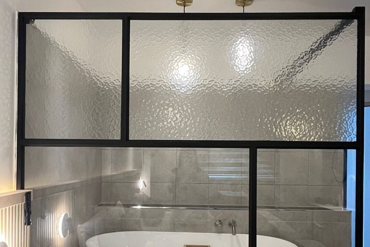 Een moderne badkamer met een vrijstaand bad, geëtste glazen panelen en een houten wastafelmeubel.