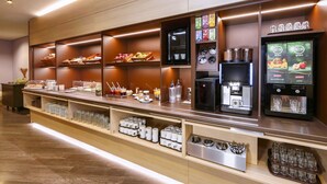 Een ontbijtbuffet in een hotel met een koffieapparaat, theeset en diverse etenswaren.