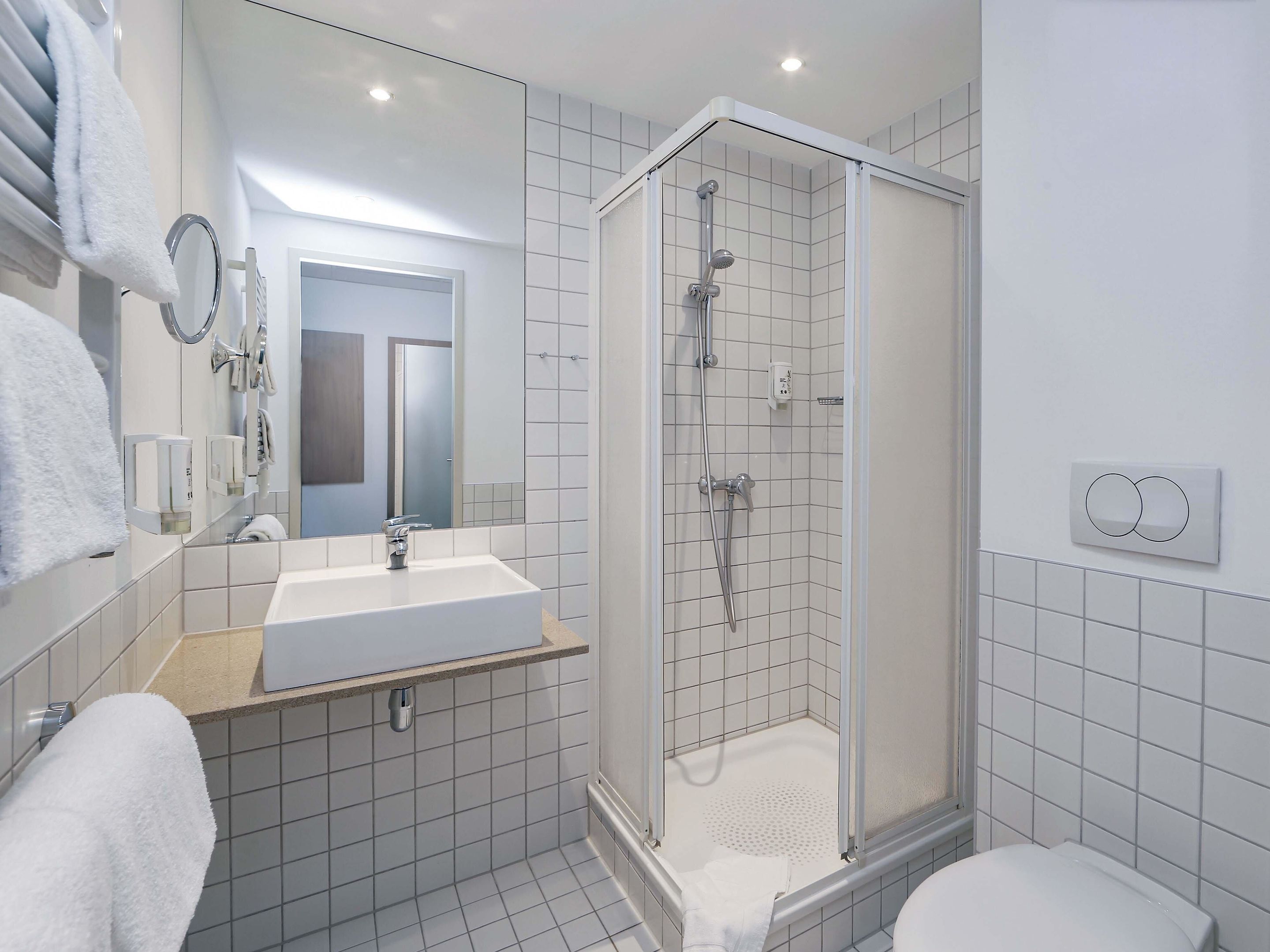 Un baño moderno con ducha de vidrio, un lavamanos blanco y un inodoro.