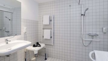 A modern bathroom with a large mirror, a sink, a handheld showerhead, and a towel rack.