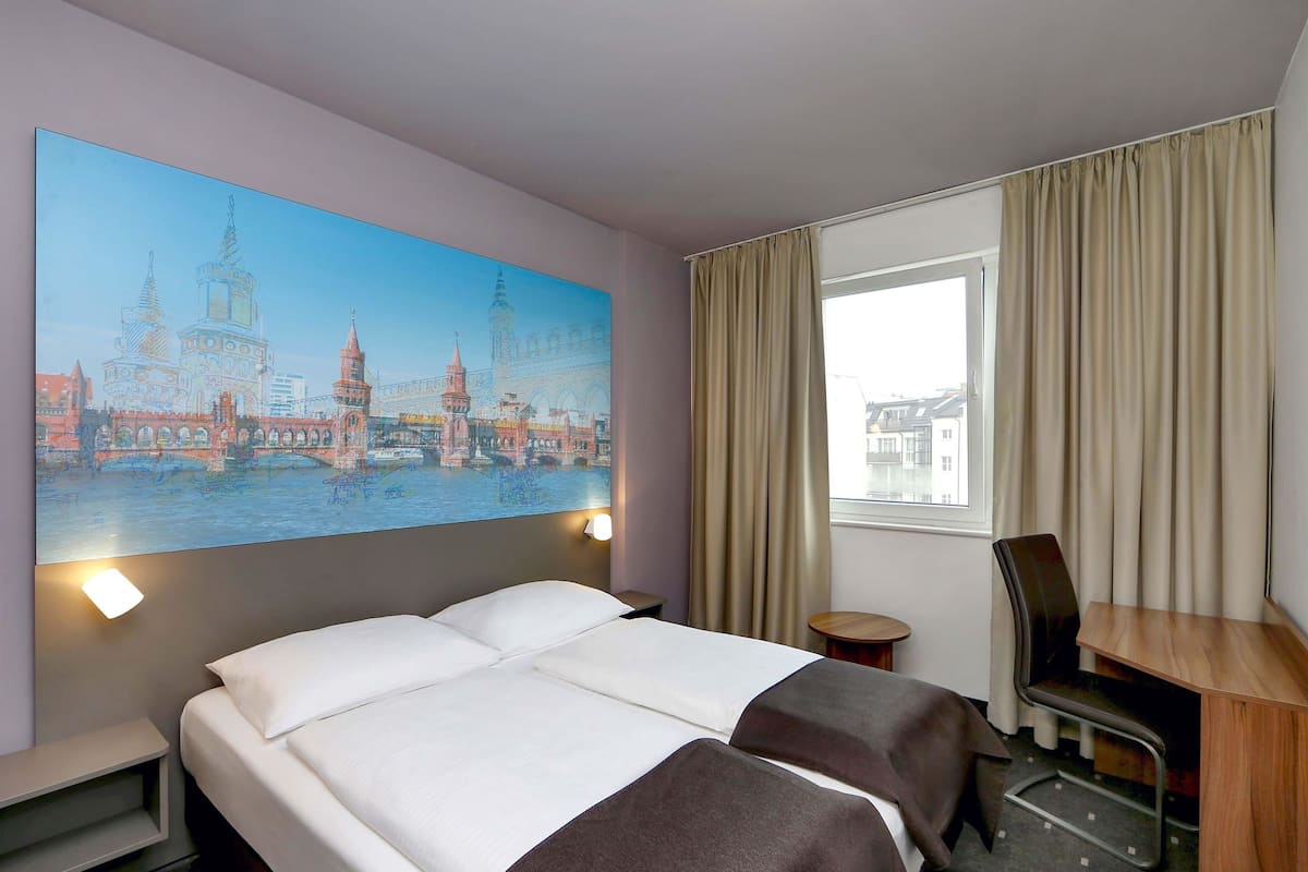 Habitació d'hotel amb un llit gran, una taula de treball, una cadira i una finestra amb cortines.