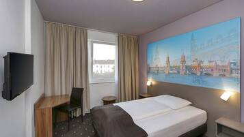 A hotel room with a bed, a desk, a chair, a TV, a window with curtains, and a painting of a cityscape.