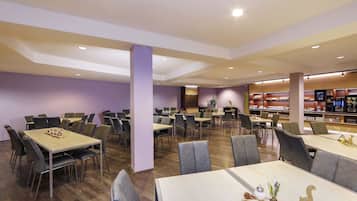 Un grand espace dédié à la salle à manger, avec plusieurs tables et chaises, une colonne centrale et, au fond, un présentoir pour les plats.
