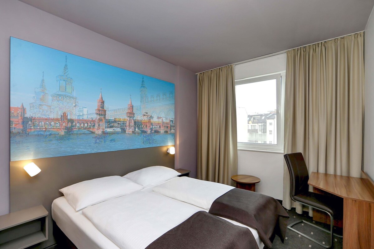 Une chambre d’hôtel avec un grand lit, un bureau, une chaise et une fenêtre avec des rideaux.