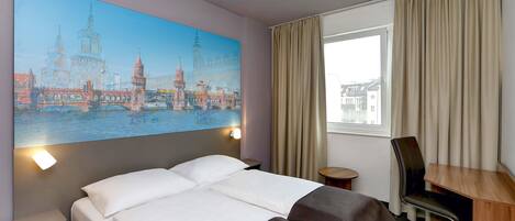 Ein Hotelzimmer mit einem großen Bett, einem Schreibtisch, einem Sessel und einem Fenster mit Vorhängen.