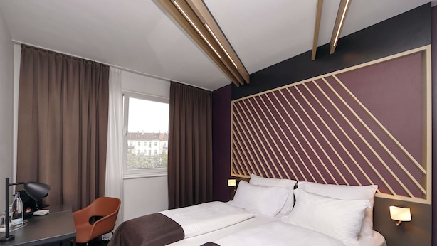 Een hotelkamer met een bed, een bureau, een stoel en een raam met gordijnen.