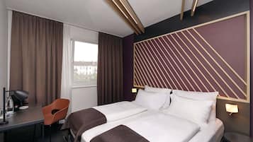 Une chambre d’hôtel avec un lit, un bureau, une chaise et une fenêtre avec des rideaux.
