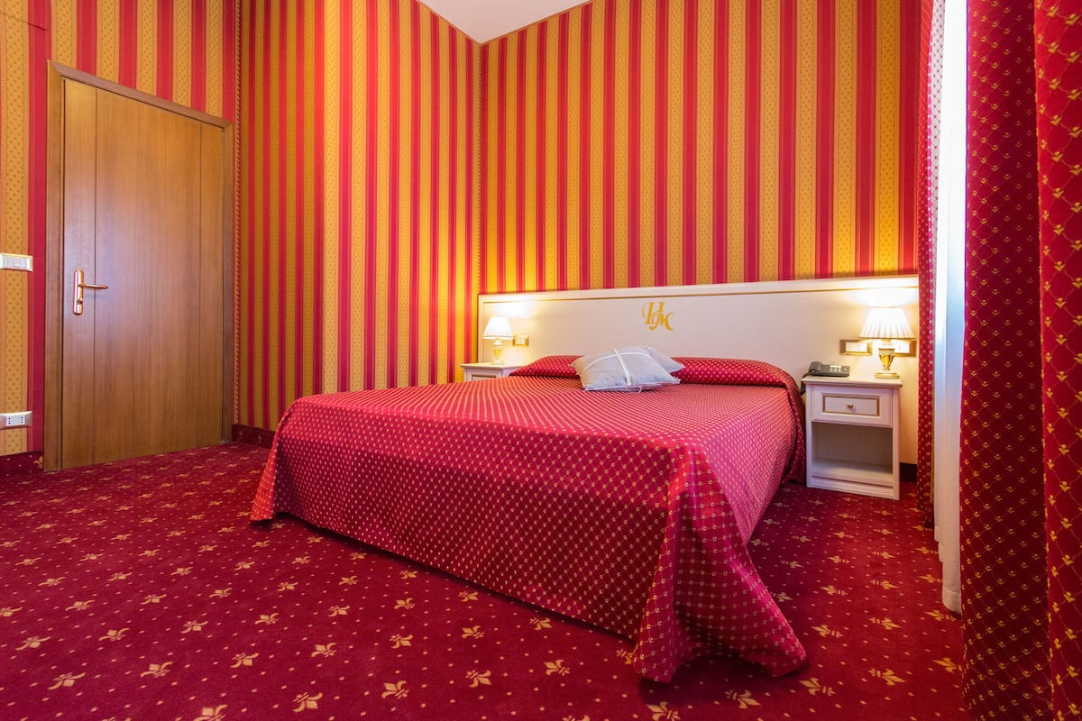 A hotel room with a large bed, striped wallpaper, and a red carpet.