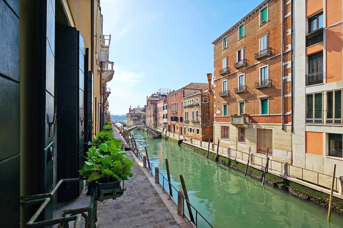 A canal with buildings on either side, a bridge in the distance, and a potted plant on the steps.