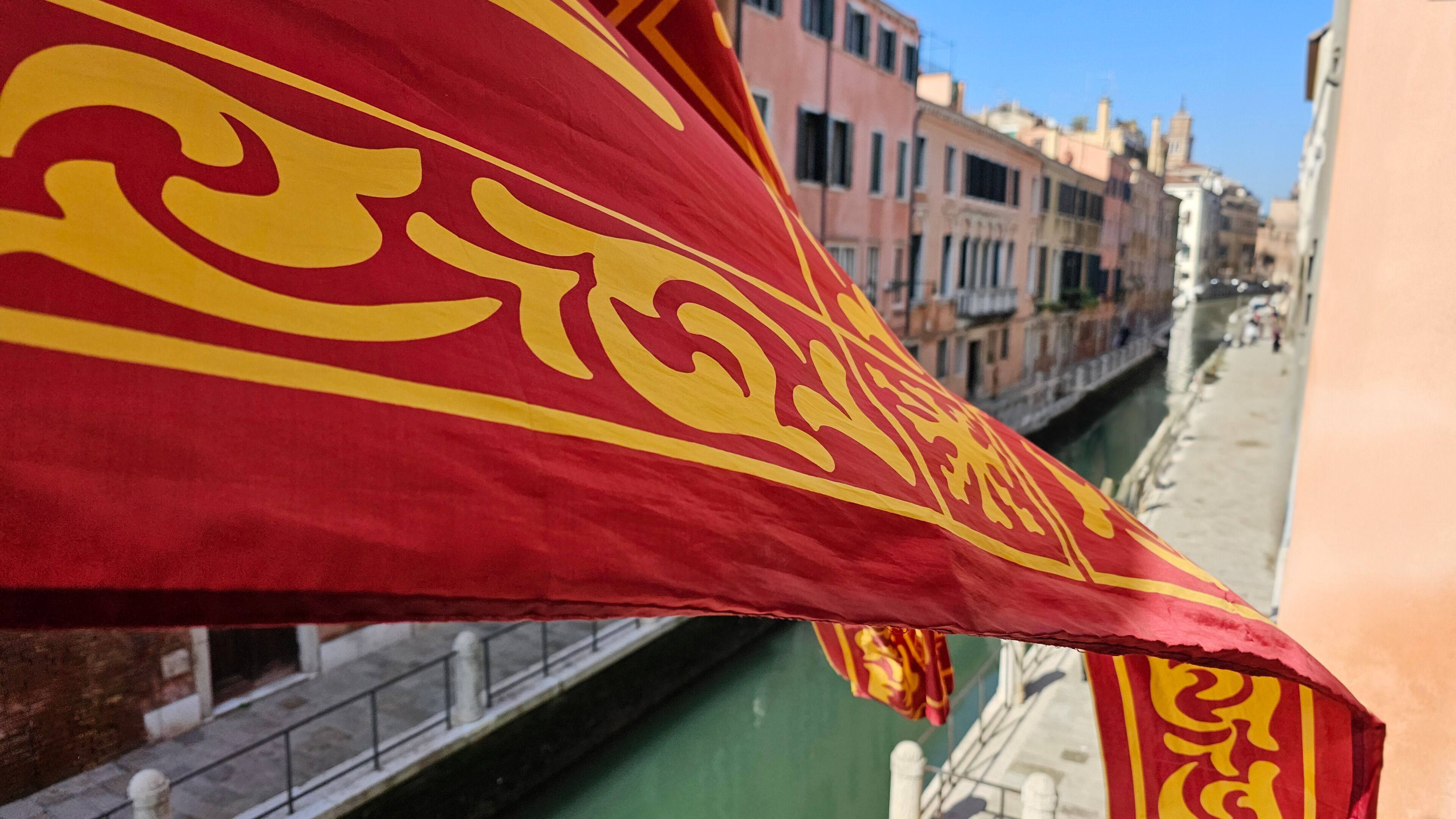 Et rødt flag med gule mønstre, en kanal og bygninger langs vandet.