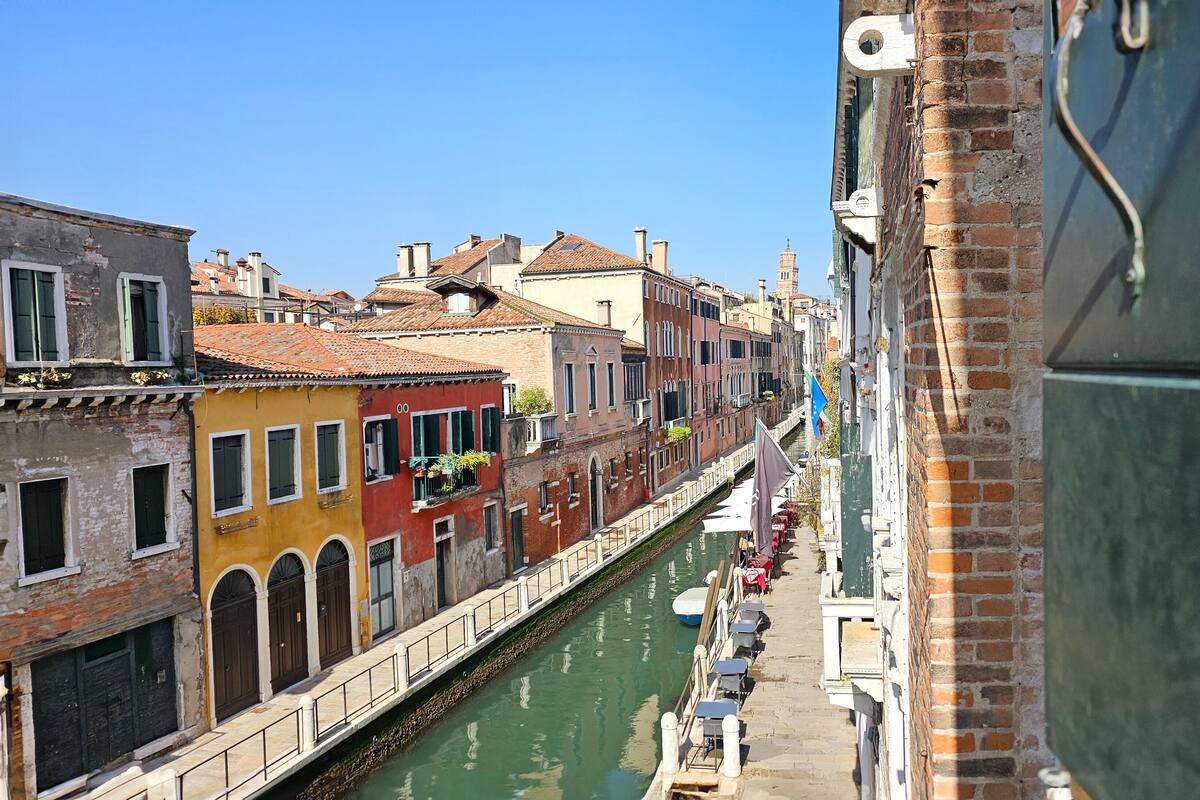 A narrow canal flanked by colorful buildings with balconies, a clear sky, and a boat docked on the water.
