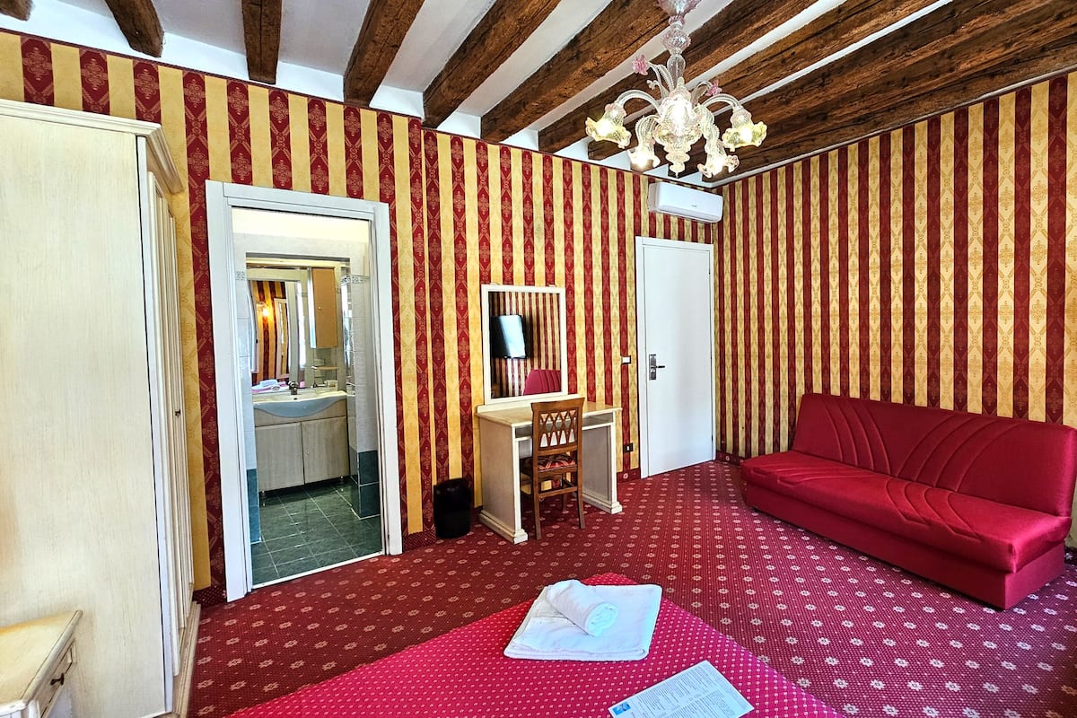 A room with striped wallpaper, a red sofa, a television, and a mirror.
