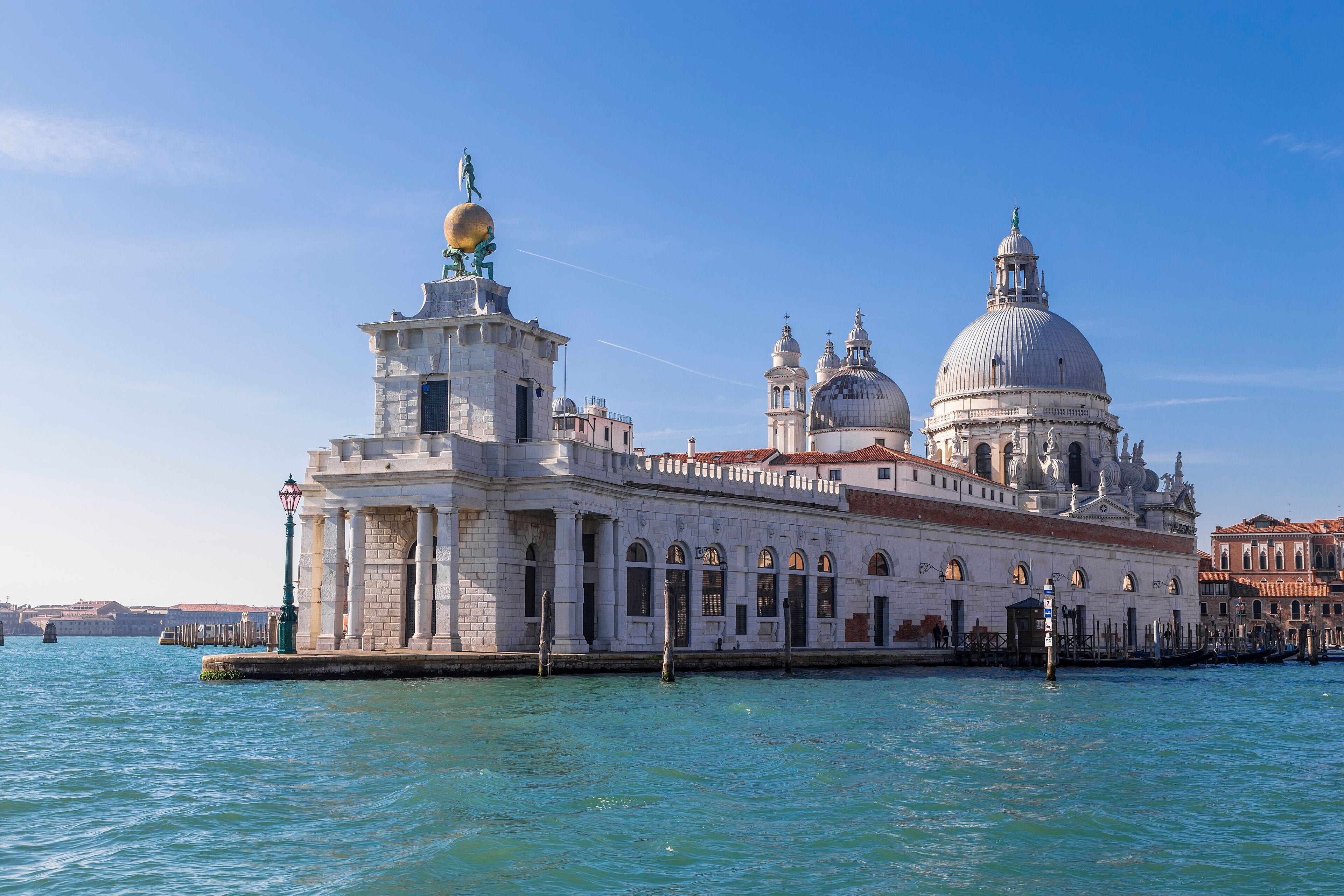 A historic building with multiple domes and a statue on top, located by a body of water.