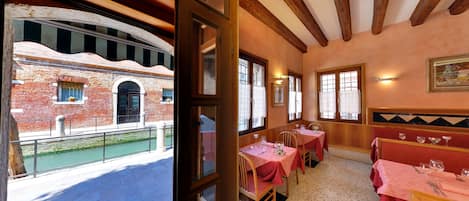 A dining area with tables set for two, a brick building with arched windows, and a balcony with a railing.