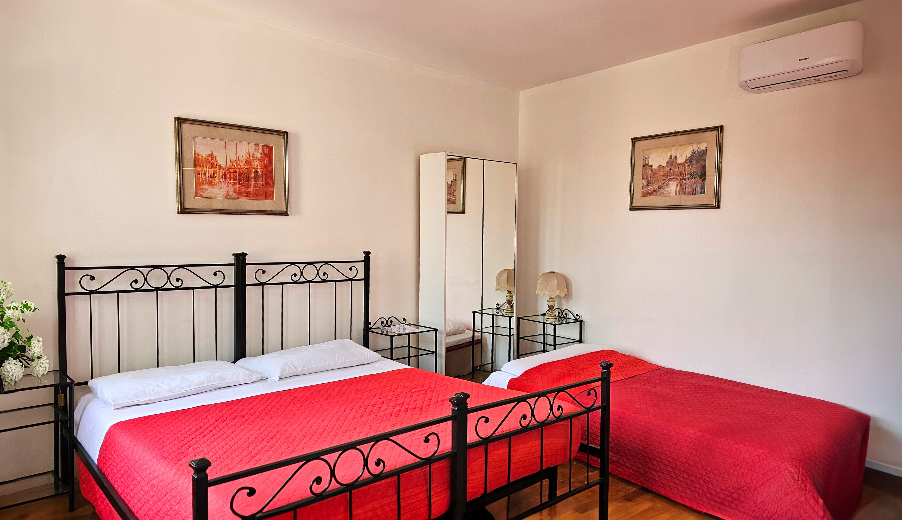A bedroom with a bed, a bedside table, a mirror, and two framed pictures on the wall.