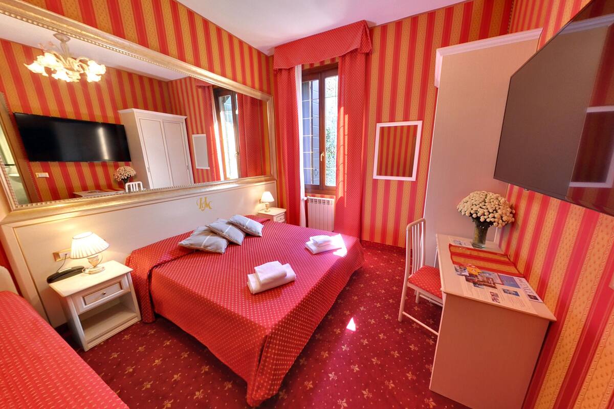 A hotel room with a large bed, a TV, a desk with a lamp, and a chair.