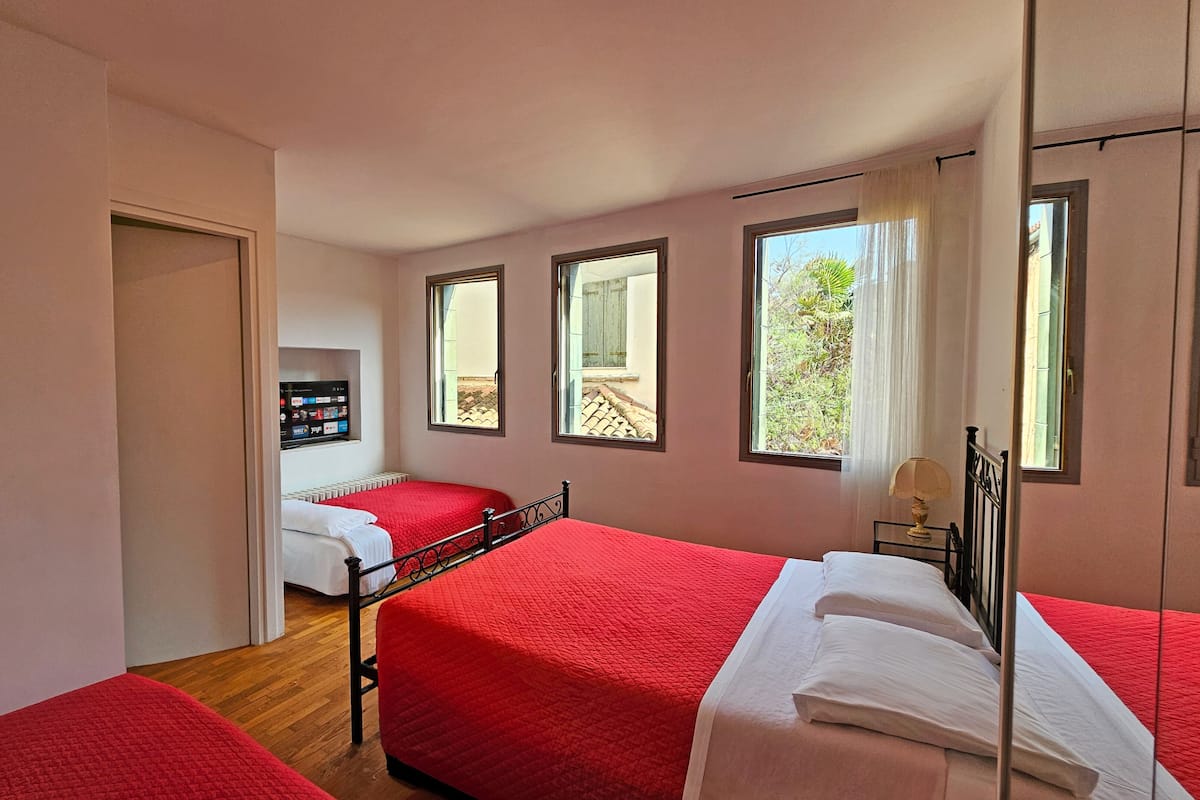 A bedroom with two beds, a TV, and large windows.