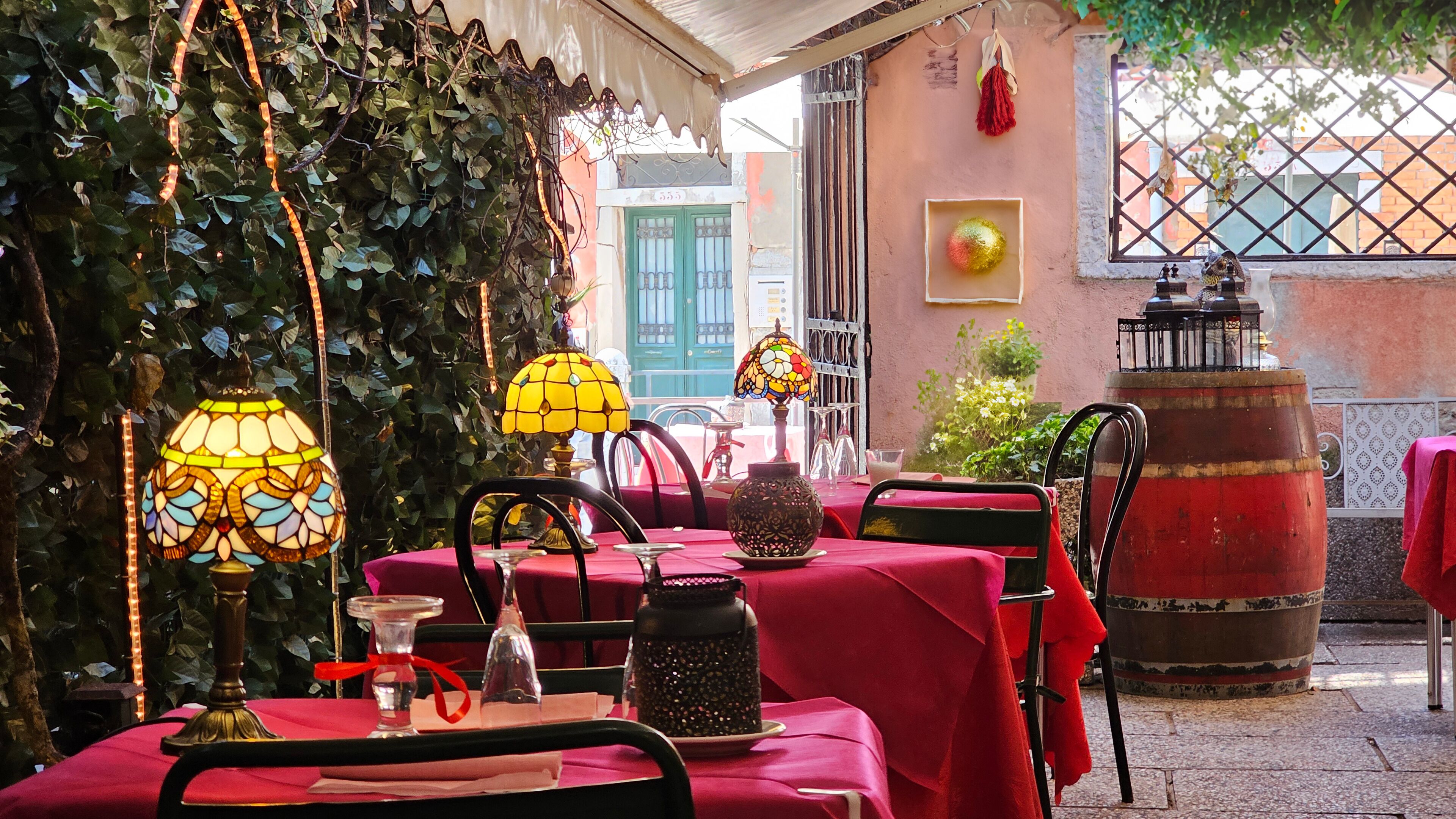 Un espace de restauration en plein air avec des tables recouvertes de nappes rouges, entourées de verdure et illuminé par des lampes décoratives.