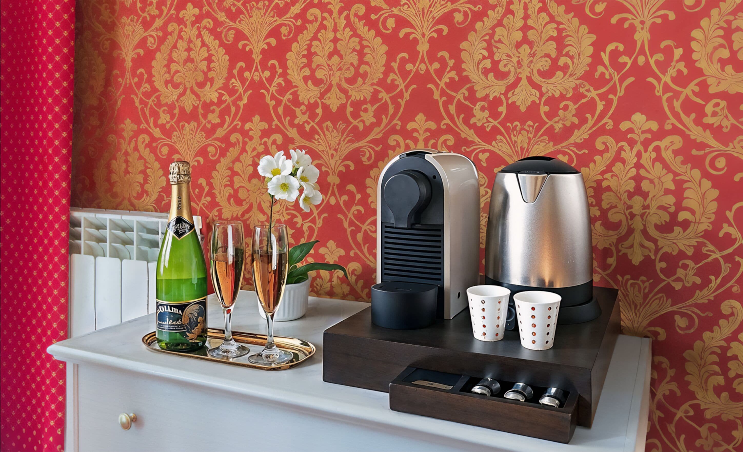 A minibar setup with a bottle of champagne, two glasses, a flower, a coffee maker, and two cups on a tray.