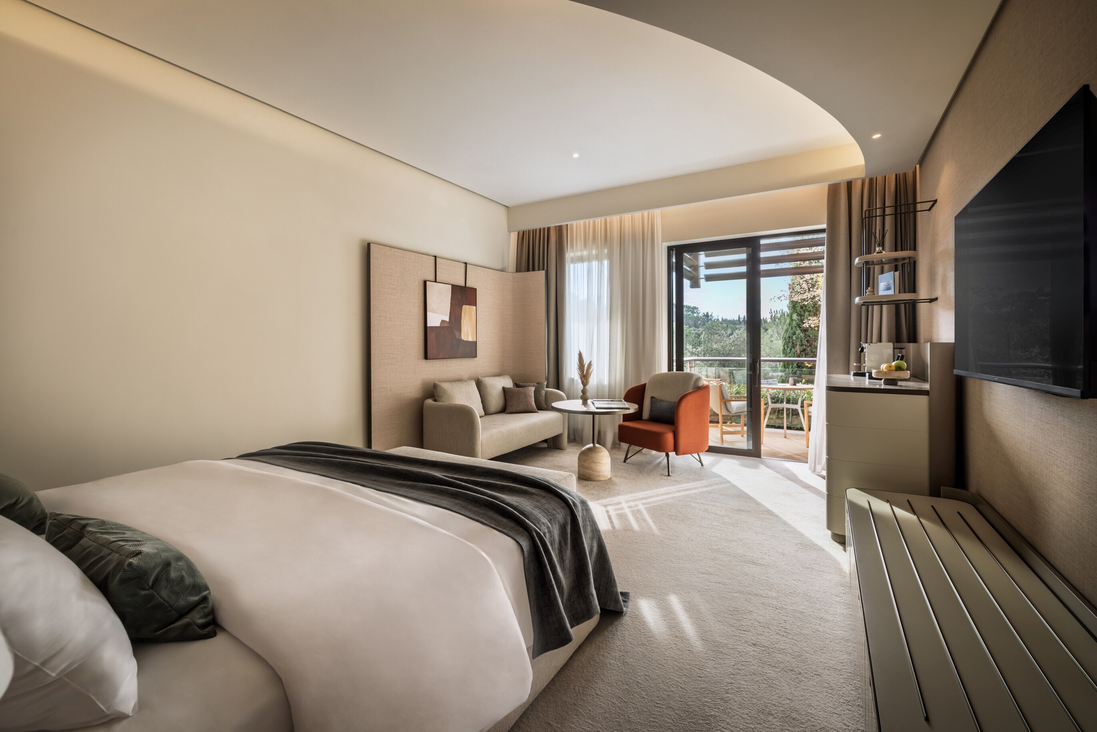 A modern hotel room with a large bed, a sofa, a small round table, and a TV mounted on the wall.