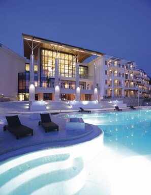 Un hotel moderno con una amplia piscina, tumbonas y una fachada bien iluminada.