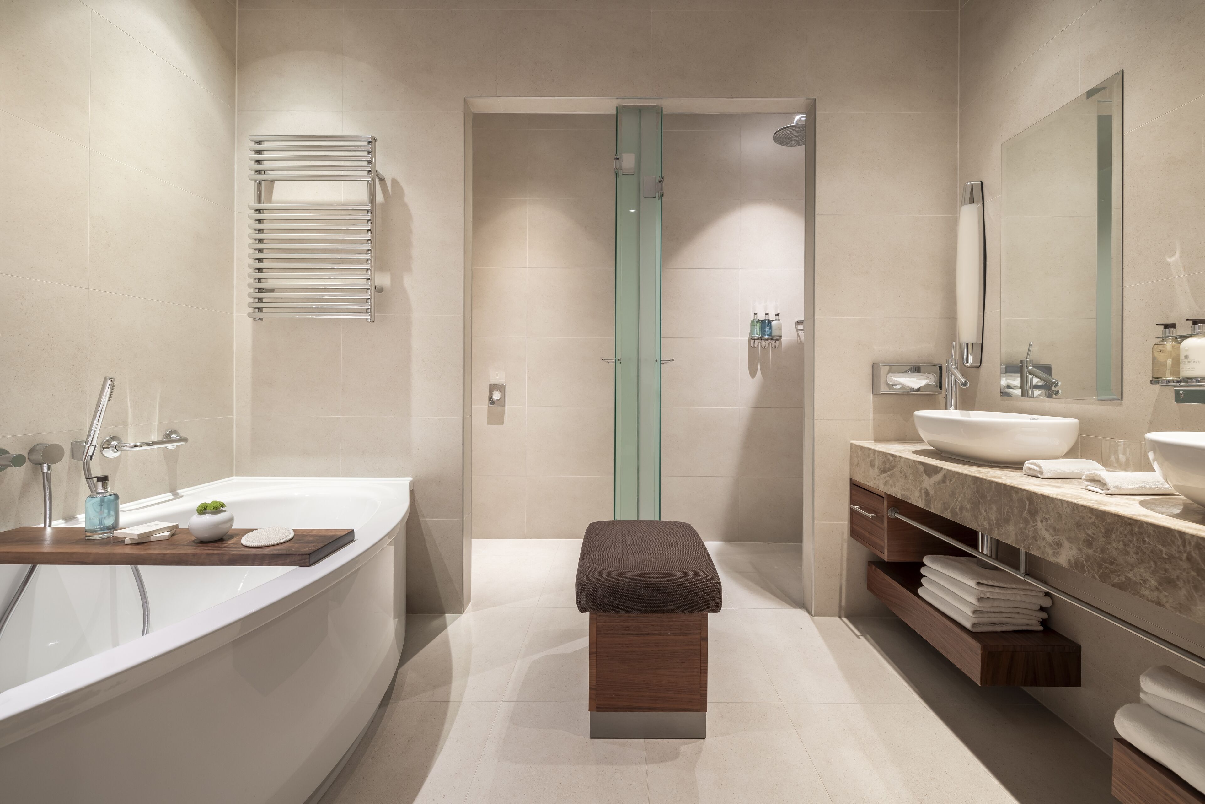 A modern bathroom with a large bathtub, a wooden bench, a sink, and a mirror.