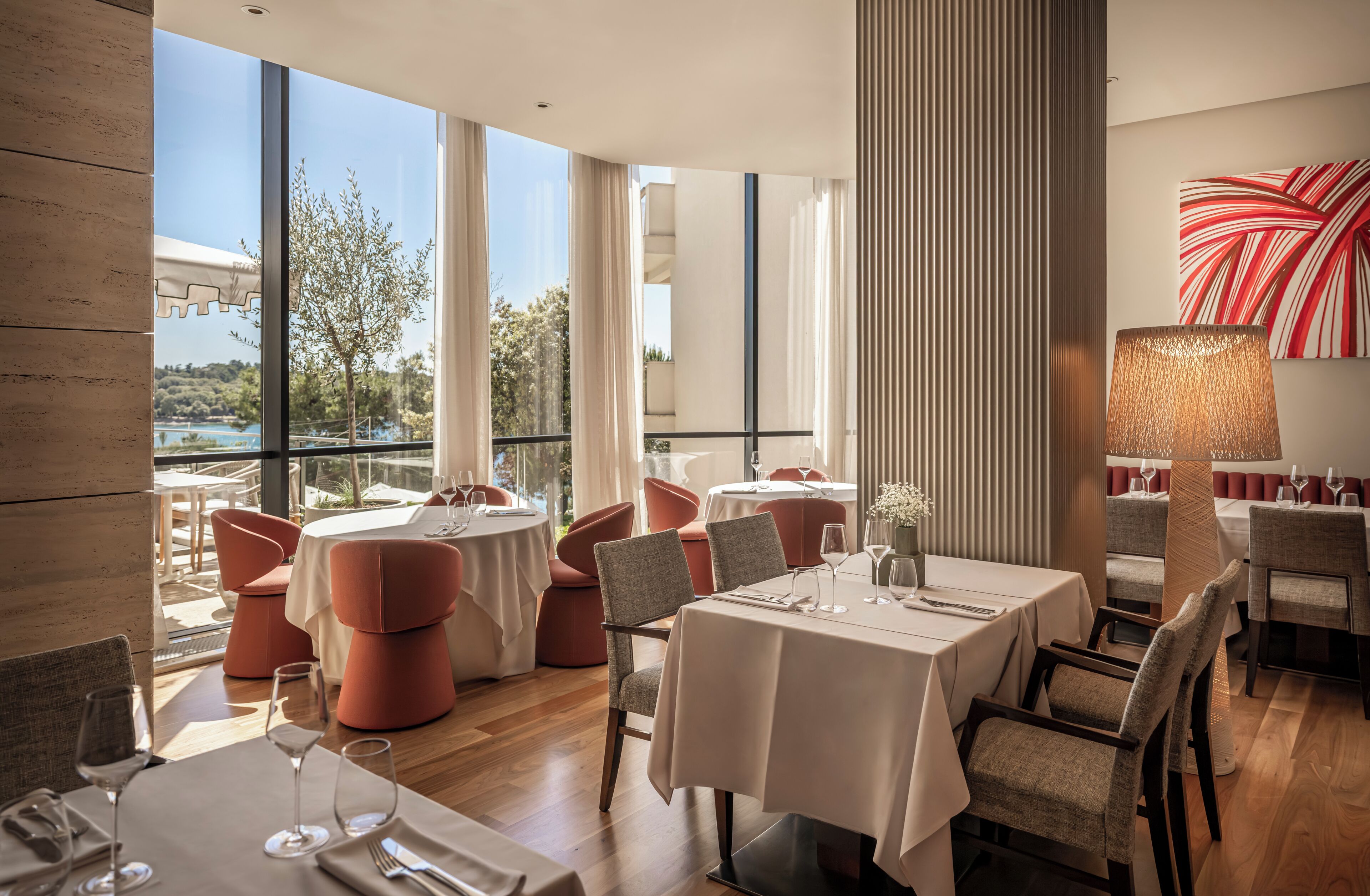 Un restaurante con mesas y sillas redondas, ventanas amplias y vistas al exterior.