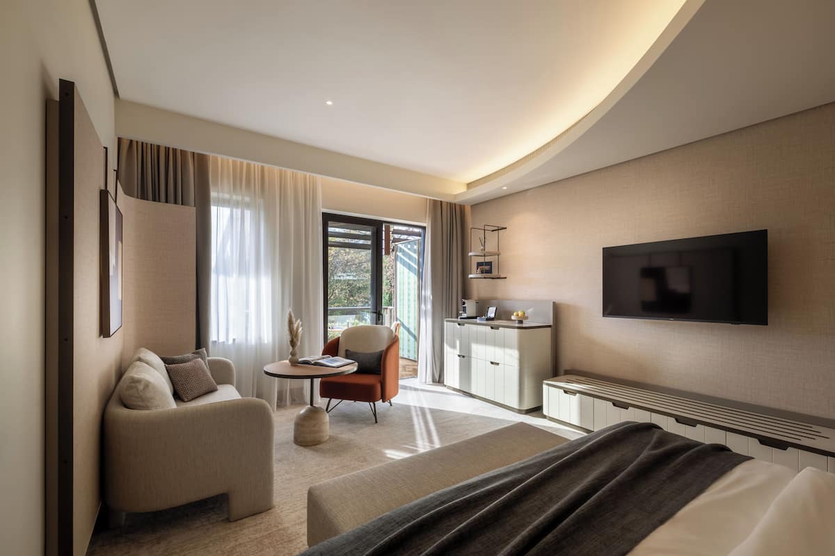 Ein modernes Hotelzimmer mit einer Couch, einem kleinen Tisch, einem Sessel, einem Fernseher und einer Küchenzeile.