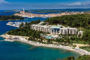 Un hotel sulla costa con diversi piani, una piscina e una spiaggia attrezzata con ombrelloni e lettini.