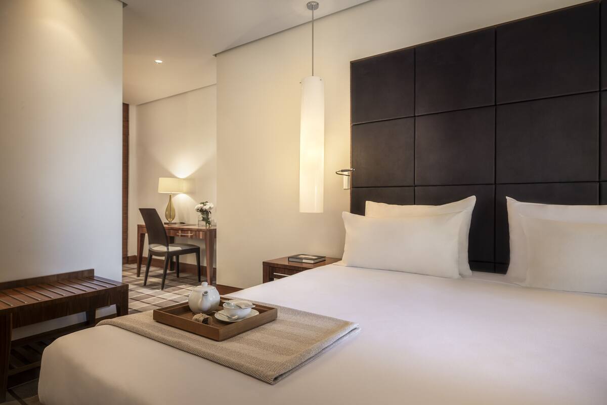 Ein modernes Hotelzimmer mit einem großen Bett, einem Nachttisch, einem Schreibtisch mit Stuhl und einer Pendelleuchte.