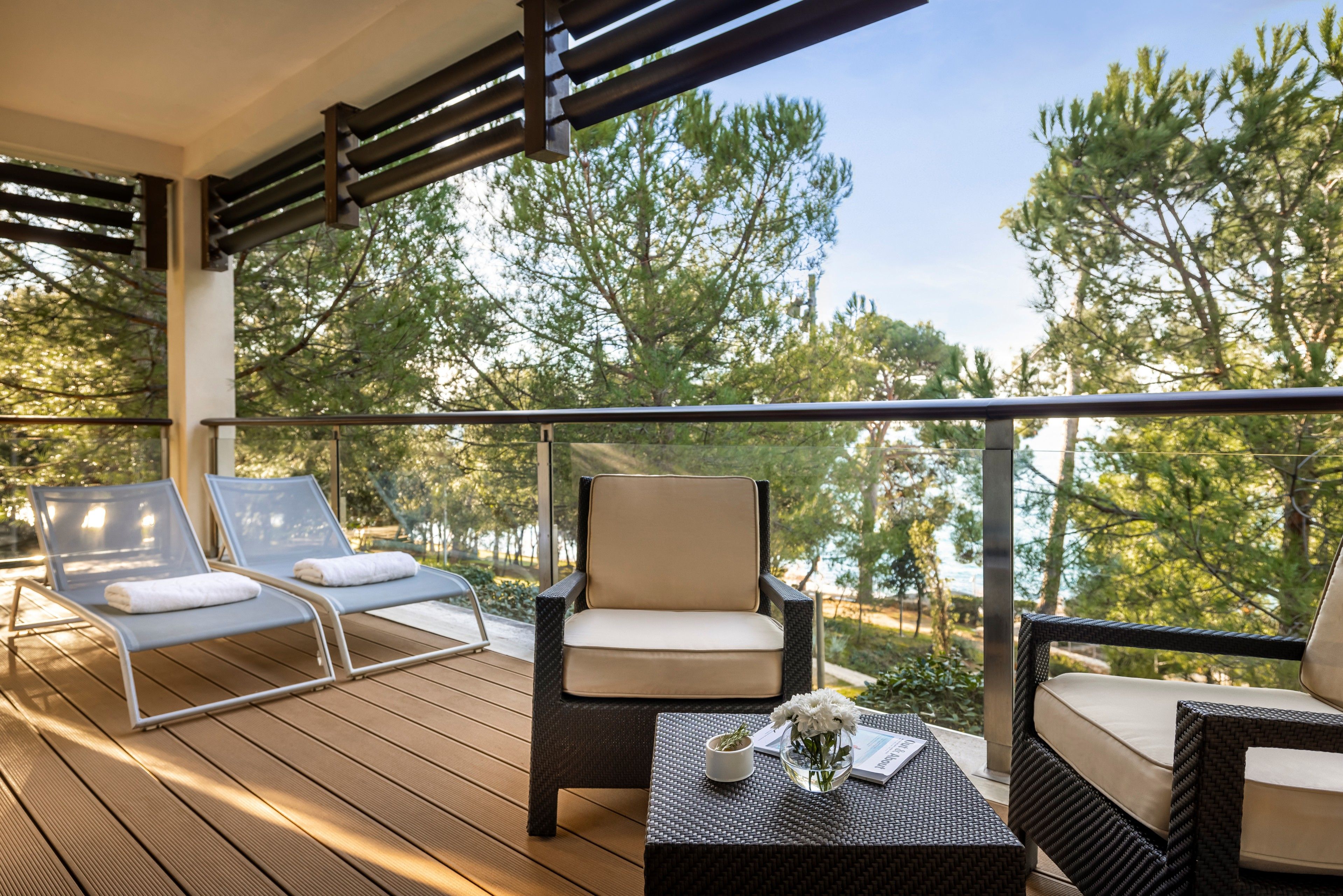 A balcony with wicker furniture, a table with a vase, and a view of trees.