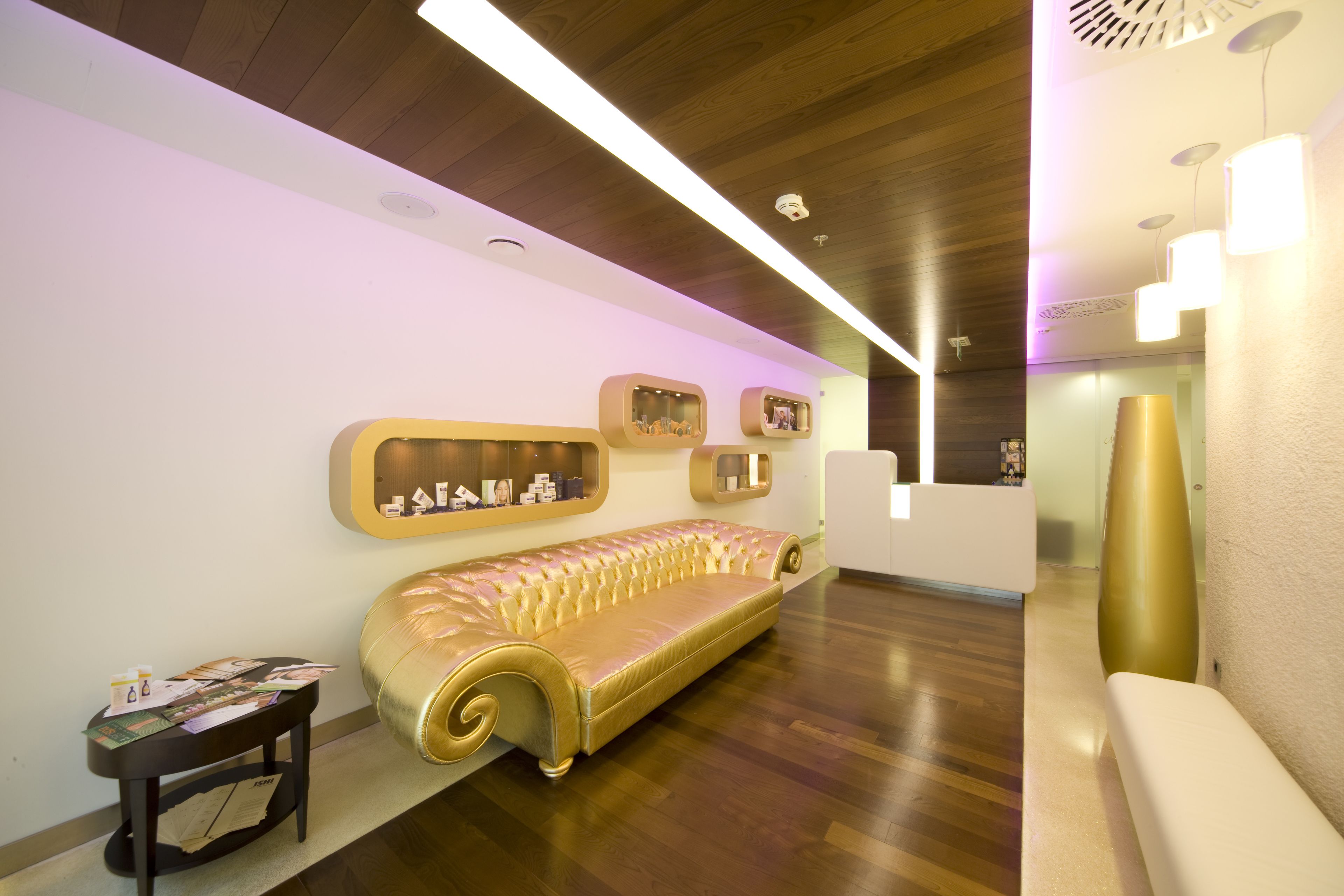 A reception area with a gold-colored sofa, a small table with papers, and a reception desk.