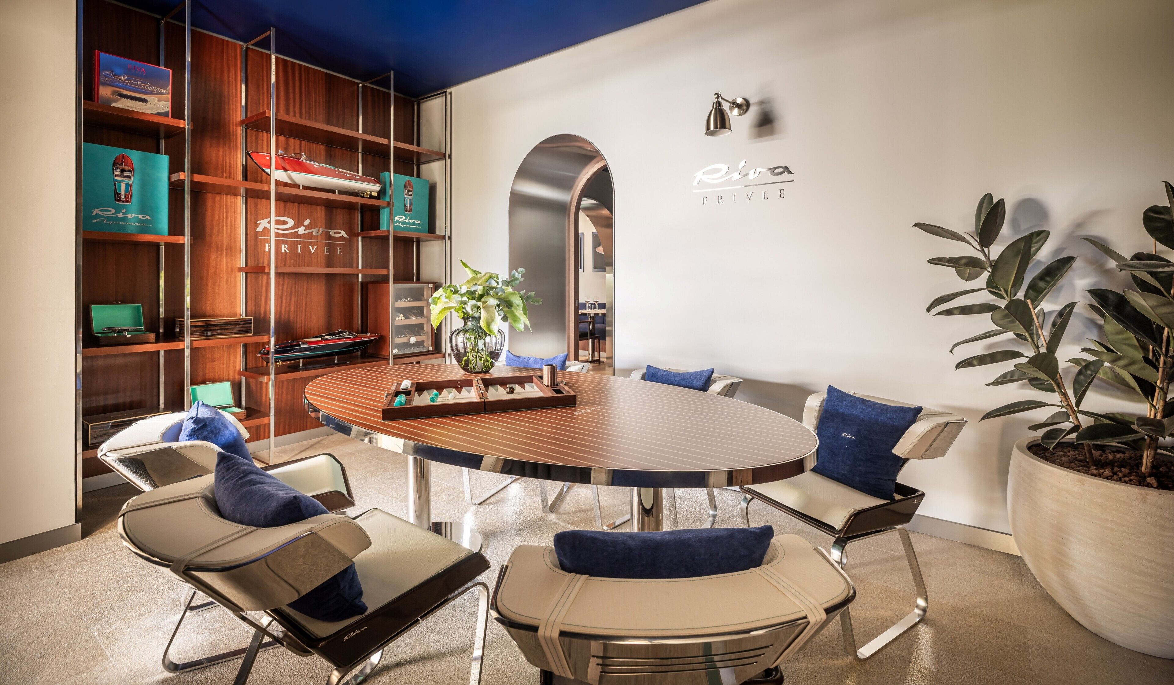 Una sala de reuniones moderna con una mesa redonda, sillas cómodas, una estantería con maquetas de barcos y una planta en maceta.