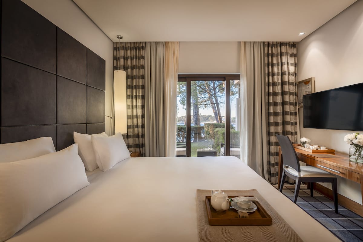 Ein Hotelzimmer mit einem großen Bett, einem Schreibtisch mit Stuhl, einem Fernseher und Blick ins Freie.