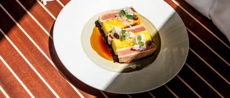 A plate of food with a slice of meat and a yellow topping, placed on a table with a striped pattern.